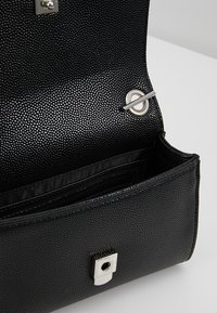 Black textured handbag with a silver snap closure and interior pockets. Features a smooth lining and structured shape.