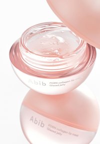 Pot rond translucide avec un couvercle rose pâle. Contient un masque à lèvres clair et brillant. L'étiquette indique « Abib PDRN collagen lip mask Glazed jelly ».