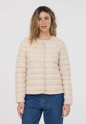 Giacca imbottita trapuntata beige con scollatura arrotondata, chiusura con bottoni, maniche lunghe e tessuto liscio, abbinata a jeans blu.
