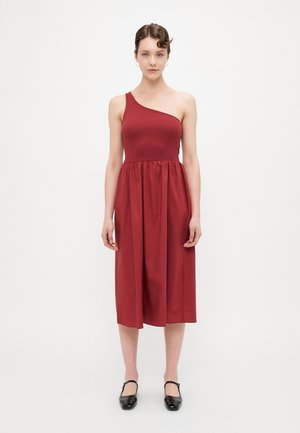 Rød one-shoulder kjole med et tettsittende topp og samlet skjørt. Laget av glatt stoff, kne-lengde, paret med svarte leiligheter.