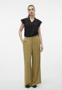 Blusa nera con texture, maniche a volant e scollatura a V, abbinata a pantaloni olive green a vita alta e gamba larga. Scarpe nere a punta.