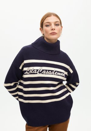Suéter de rayas en azul marino y crema de gran tamaño, con un cuello alto y texto bordado "LolaCasademunt". Tejido de punto texturizado.