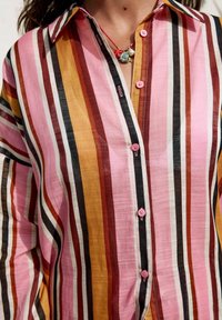Gestreepte shirt met verticale patronen in roze, oranje, zwart en wit. Inclusief een knoopsluiting en zachte, lichte stof.