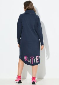 Abito oversize blu navy con colletto alto e lettering rosa "KLITTER" sull'orlo. Realizzato in tessuto morbido, presenta maniche lunghe.