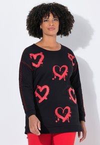 Zwarte sweatshirt met rode spuitverf hartontwerpen. Lange mouwen met rode decoratieve stiksel langs de zijkanten. Relaxed fit.