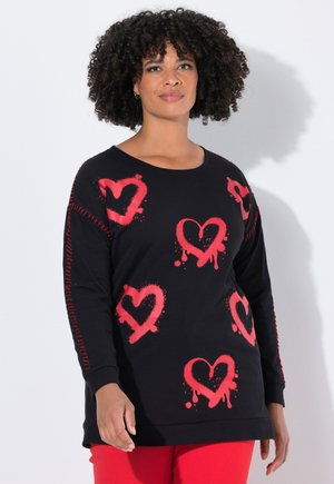 Sweatshirt noir avec des designs de cœurs peints en rouge. Manches longues avec des couture décoratives rouges sur les côtés. Coupe décontractée.