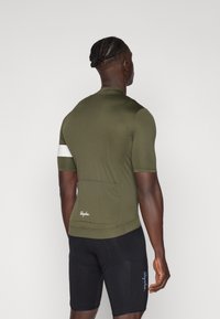 Cămașă de ciclism verde măsliniu cu mânecă scurtă, cu dungi reflective albe, buzunare la spate și detalii cu logo alb și albastru pe pantaloni scurți negri.