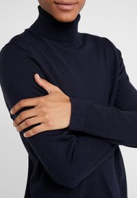 Mörkblå polotröja i mjukt stickat material, med långa ärmar och en figursydd design med ribbade muddar för en åtsittande look.