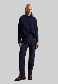 Suéter de gran tamaño en azul marino, con tejido texturizado, y pantalones de pana azul marino con un ajuste relajado. Unos zapatos marrones con cordones completan el conjunto.