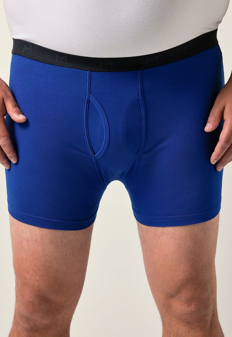 Blå boxerkalsonger tillverkade av elastiskt tyg med svart elastisk midjeband som har bokstaven "M". Inkluderar en framöppning och en snug passform.