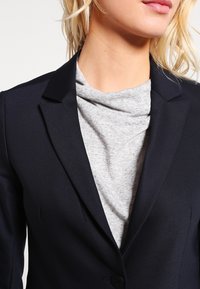 Navyblazer med en slät, skräddarsydd design med slagkrage och en knappstängning, lager på ett ljusgrått topp med fällkrage.