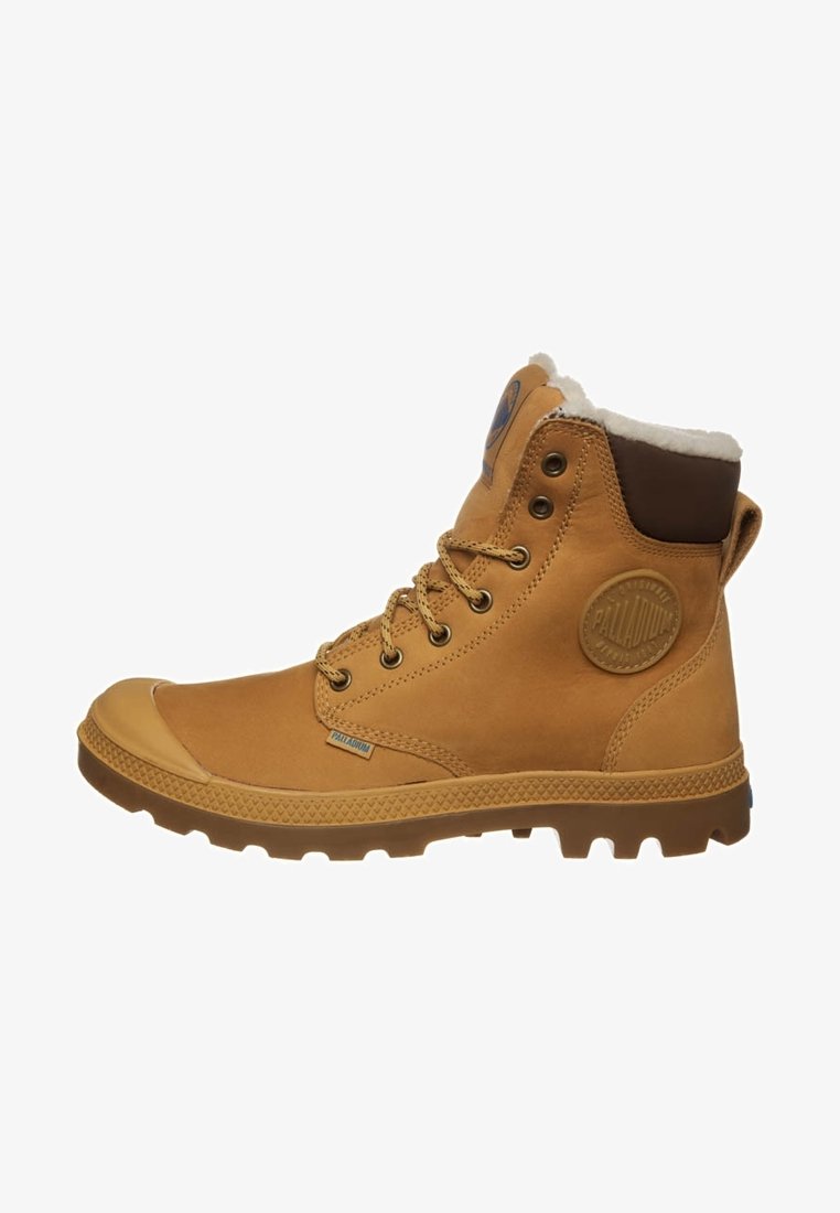 Botte en cuir beige à lacets avec col matelassé, semelle robuste et patch rond avec logo sur le côté, conçue pour une utilisation en extérieur.