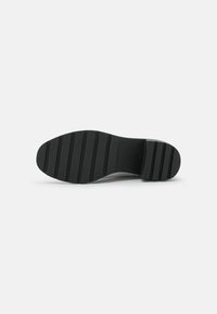Semelle de chaussure en caoutchouc noir avec des rainures et des crêtes horizontales, présentant un devant lisse et une forme de bout arrondi pour une traction et une stabilité.
