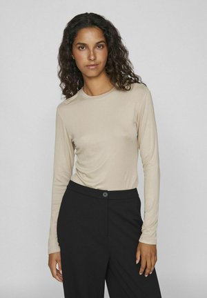 Langærmet beige top lavet af et glat stof, parret med sorte bukser med en knaplukning foran. Enkel design og pasform.