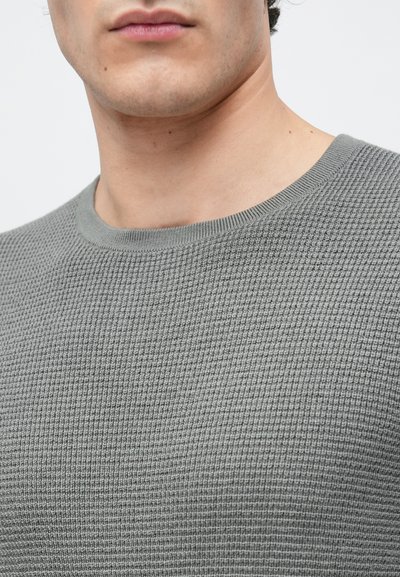 Šedý pletený svetr s texturovaným vaflovým vzorem. Má kulatý výstřih a měkkou, elastickou tkaninu. Detailní pohled na horní část trupu.