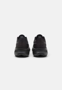Chaussures de sport noires avec une tige texturée, un talon arrondi et une semelle en caoutchouc. Design minimaliste avec des accents réfléchissants et un col rembourré.