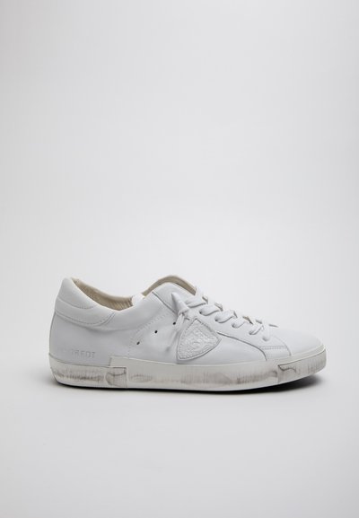 Baskets en cuir blanc avec bout rond, design à lacets, détails perforés et accents subtils de saleté sur la semelle en caoutchouc. Logo sur le côté.
