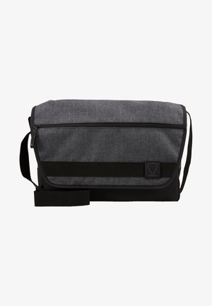 Sac messenger gris avec un corps en tissu texturé, accents noirs, une bandoulière et une poche frontale zippée. Comprend un patch de logo.