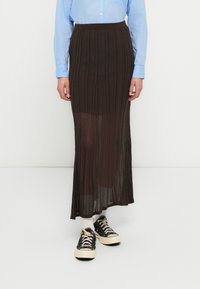 Jupe longue plissée marron en matière transparente, associée à une chemise bleu clair et des baskets noires avec des lacets crème.