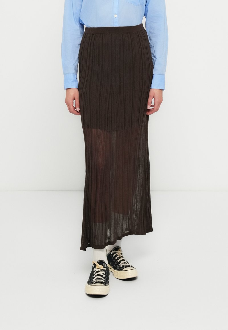 Jupe longue plissée marron en matière transparente, associée à une chemise bleu clair et des baskets noires avec des lacets crème.