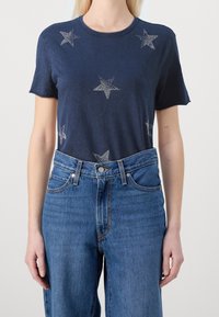 Camiseta de algodón azul marino con gráficos de estrellas plateadas, mangas cortas y cuello redondo, combinada con jeans de mezclilla azul de cintura alta.