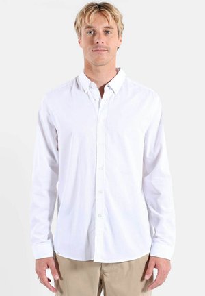 Chemise blanche à manches longues avec col et boutons, en tissu lisse, présentant une coupe décontractée et des détails de couture subtils.