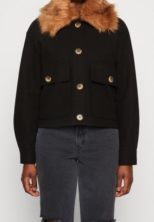 Zwarte jas met knopen, grote bruine nepbonten kraag en twee voorzakken met kleppen, gedragen met donkergrijze denim shorts.