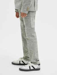 Ljust grå linnekostymbyxor med rak passform, kombinerat med vita sneakers med svarta och grå detaljer. Knappar synliga på jackan.