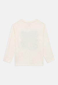 Μπλούζα με μακριά μανίκια σε εκρού χρώμα, με μια ελαφρώς ορατή γραφική παράσταση στο πίσω μέρος, απλωμένη επίπεδη σε απλό ανοιχτόχρωμο φόντο.