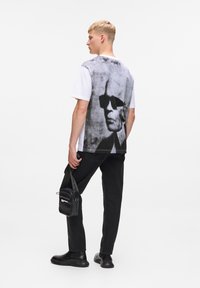 Weißes Baumwoll-T-Shirt mit einem großen Graustufenbild auf der Rückseite, kombiniert mit schwarzen Jeans und einer kleinen schwarzen Umhängetasche.