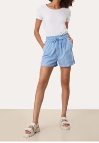 Světle modré pruhované šortky s elastickým pasem, předními kapsami a zavazovacím detailem, doplněné bílým tričkem s krátkým rukávem a bílými sandály.