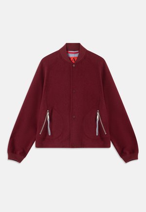 Burgundy takki, jossa on pyöreä kaulus, napitus ja kaksi vetoketjullista taskua. Valmistettu teksturoidusta kankaasta, jossa on kontrastivärinen vuori.