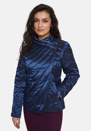 Navyblauwe gewatteerde jas met hoge kraag, voorzien van diagonale stiksels en zijzakken. Gemaakt van een glanzende, lichtgewicht stof.