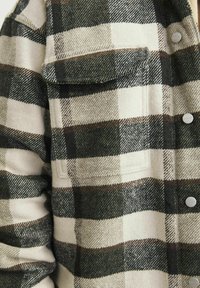Camicia di flanella a scacchi in crema e verde scuro. Presenta una tasca sul petto, bottoni e un tessuto morbido e testurizzato.