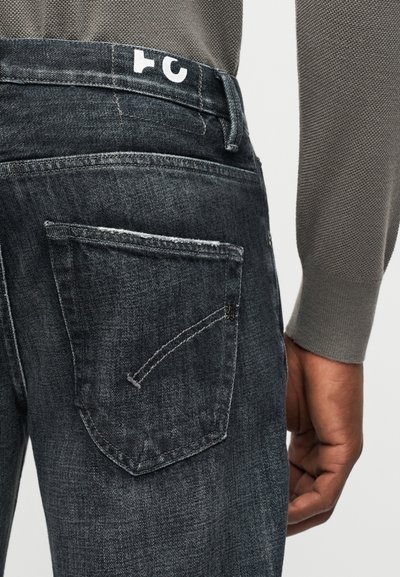 Κοντινό πλάνο ενός ατόμου που φοράει σκουρόγκρι τζιν και γκρι μακρυμάνικη μπλούζα με υφή, δείχνοντας την πίσω τσέπη και το χέρι.