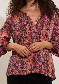 Blusa floreale multicolore con scollatura a V, dettagli arricciati sulle spalle e polsini elastici. Realizzata in tessuto leggero con una vestibilità fluida.