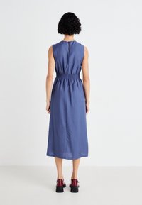 Sleeveless blue dress with a relaxed fit, gathered waist, and knee-length cut. Features a back button closure and textured fabric.
