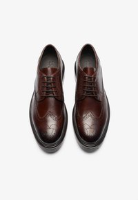 Zapatos de vestir de cuero marrón con detalles de brogue, diseño con cordones, punta redonda y suela de goma negra contrastante.