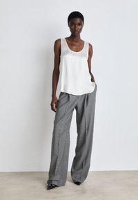 Valkoinen satiinitoppi, jossa on pyöreä pääntie, yhdistettynä harmaisiin raidallisiin leveälahkeisiin housuihin, joissa on rento istuvuus ja eturypytykset.