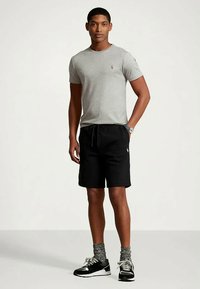 Šedé tričko s krátkým rukávem s malým logem, doplněné o černé šortky, černo-bílé tenisky a šedé ponožky s vzorem.