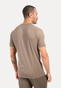 Camisa de manga corta y cuello redondo en un material beige suave. Presenta una textura lisa y un corte regular, con mangas raglán para mayor movilidad.