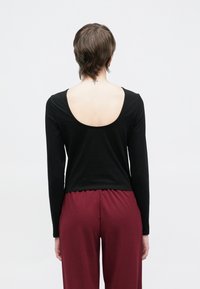 Μαύρο τοπ με μακριά μανίκια και στρογγυλή πλάτη, κατασκευασμένο από απαλό υλικό. Συνδυάζεται με παντελόνι με ελαστική μέση σε βυσσινί χρώμα.