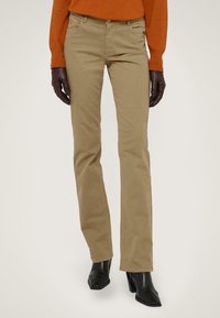 Pantalones de algodón caqui con un corte recto, cinco bolsillos y cierre de botón, combinados con botas negras de tobillo y un suéter naranja.