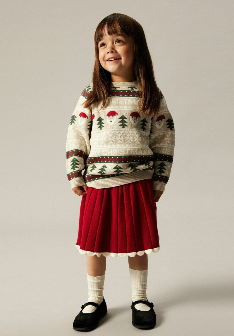 Crème brei sweater met kerstthema patronen, rode flared rok, witte kniekousen en zwarte Mary Jane schoenen. Schone achtergrond.