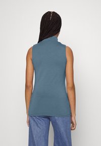 Top senza maniche, con collo alto in morbido jersey blu, dal taglio aderente, abbinato a pantaloni in denim blu a vestibilità ampia.