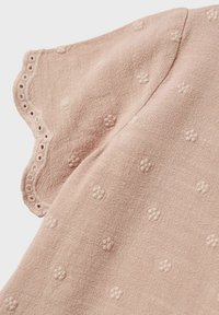 Top in cotone rosa chiaro con scollatura ondulata, caratterizzato da ricami floreali a trama e un tessuto morbido, leggermente stropicciato.