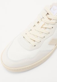 Fehér sneaker texturált hálós anyaggal és sima bőrrel. Beig színű fűzőkkel, diszkrét varrással és párnázott talppal rendelkezik. A logó a nyelvén található.