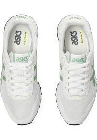 Vita atletiska skor med gröna accenter, med ett meshöverdrag, rund tå och strukturerad sula. Snören är trädde genom sex ögla.