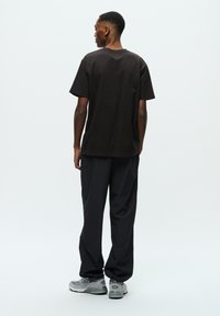 Black cotton T-shirt with a crew neckline, paired with loose gray pants. Notable details include a relaxed fit and minimalistic design.