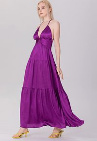 Robe maxi violette avec un corsage ajusté, un col halter et une jupe à volants. Elle présente un accent à boutons à la taille et une silhouette fluide.
